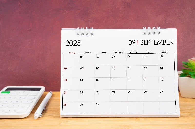 September 2025 white calendar and calculator with pen on the table.